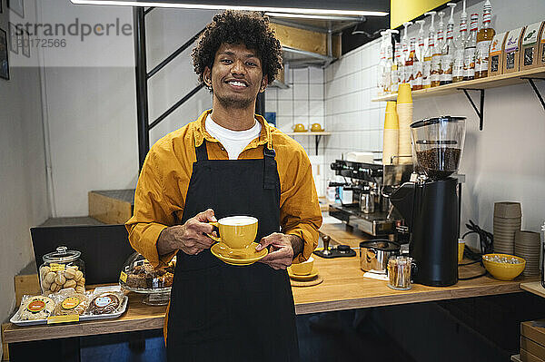 Lächelnder Barista hält eine Tasse Kaffee neben der Theke