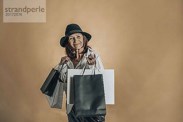 Lächelnde ältere Frau mit Einkaufstüten vor brauner Wand