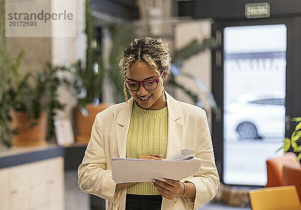 Lächelnde junge Geschäftsfrau liest Dokumente im Büro