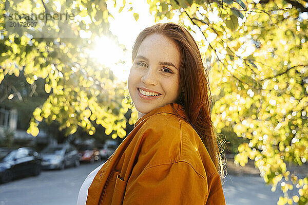 Lächelnde Frau an einem sonnigen Tag in der Nähe eines Baumes im Herbst