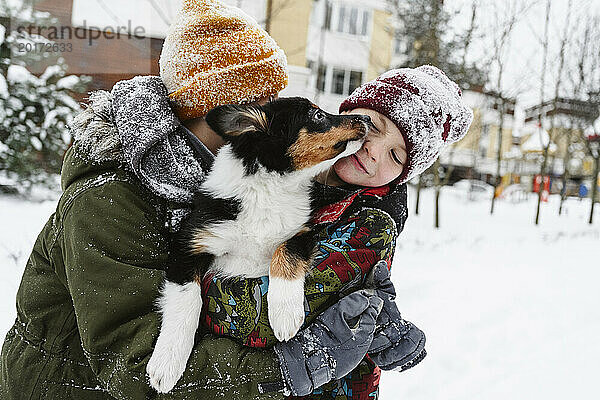 Verspielte Geschwister halten ihren Hund im Schnee zusammen