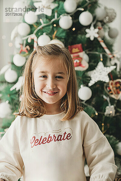 Smiling girl standing in front of Christmas tree at home