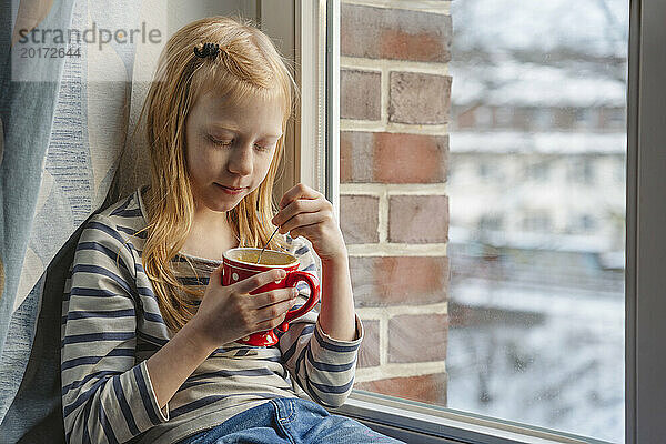 Rothaariges Mädchen hält Tasse am Fenster zu Hause