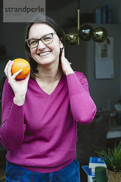 Glückliche Frau hält frische Orange in der Nähe der Tür