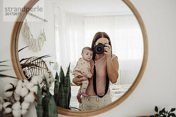 Mutter trägt ihr kleines Mädchen und fotografiert zu Hause mit der Kamera