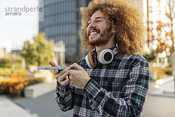 Glücklicher Mann mit lockigem Haar  Smartphone und kabellosen Kopfhörern