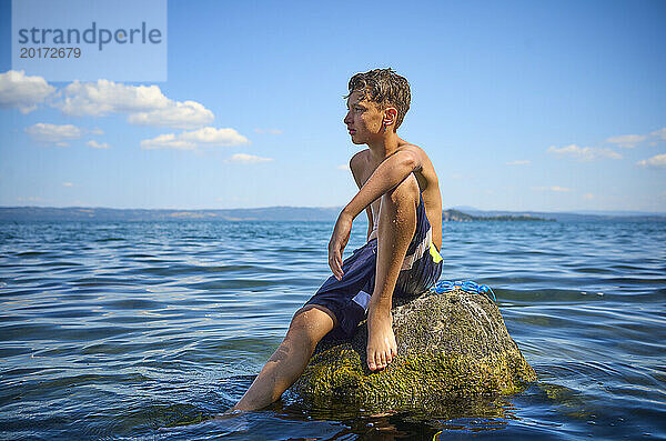 Junge sitzt auf einem Felsen im Bolsenasee  Italien