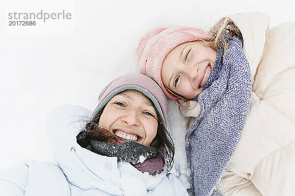 Glückliche Mutter und Tochter liegen im Winter auf Schnee
