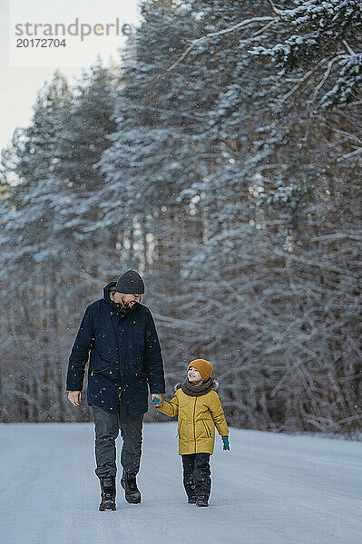 Mann hält Händchen und geht mit Sohn im Winterwald spazieren