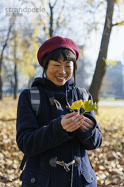 Lächelnde Frau hält Blätter im Park