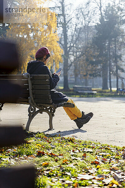 Frau sitzt auf Bank und benutzt Smartphone im Park