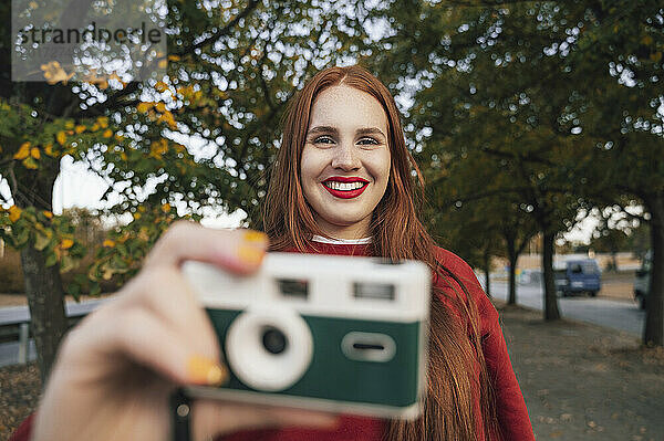 Rothaarige Frau hält Kamera im Herbstpark