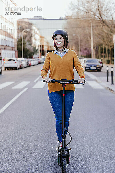 Glückliche Frau steht mit Elektroroller auf der Straße