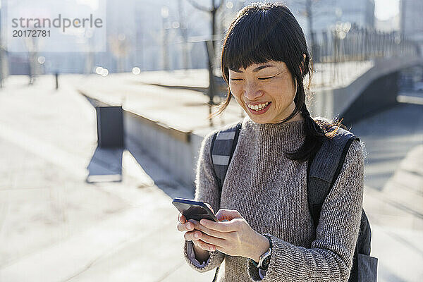 Lächelnde Frau  die an einem sonnigen Tag ihr Mobiltelefon benutzt