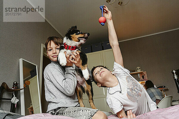 Siblings playing with dog on bed