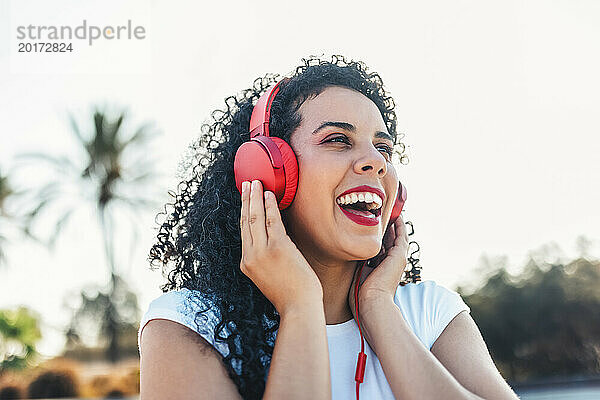 Fröhliche Frau  die im Skateboardpark Musik über kabelgebundene Kopfhörer hört