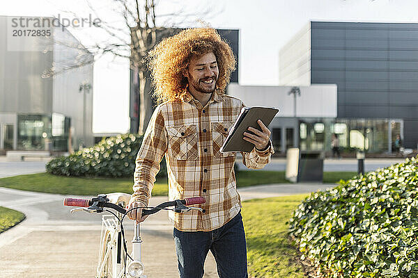 Glücklicher Mann benutzt Tablet-PC mit Fahrrad auf Fußweg