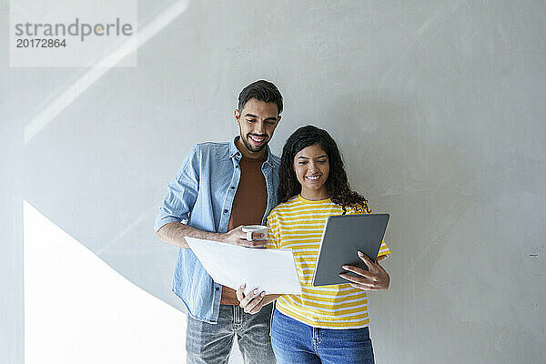 Glückliches Paar nutzt Tablet-PC und analysiert den Bauplan im neuen Zuhause
