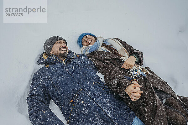 Verspieltes reifes Paar hält Händchen und liegt im Schnee im Park