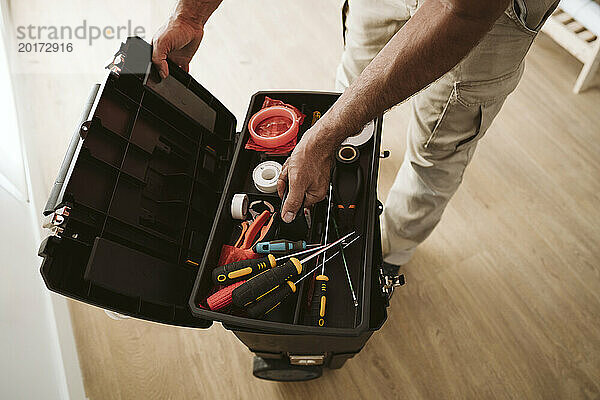 Mature technician picking up tools from box at home