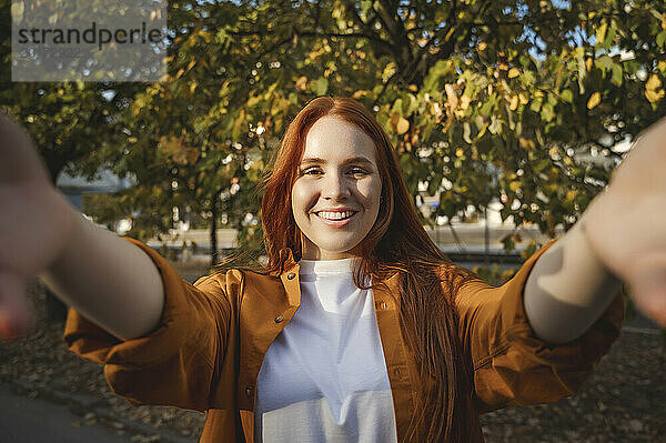 Lächelnde Frau macht im Herbst ein Selfie in der Nähe eines Baumes