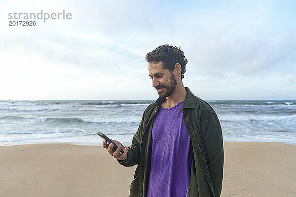 Smiling man using mobile phone at beach