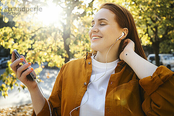 Lächelnde Frau  die im Herbst Musik über kabelgebundene In-Ear-Kopfhörer hört