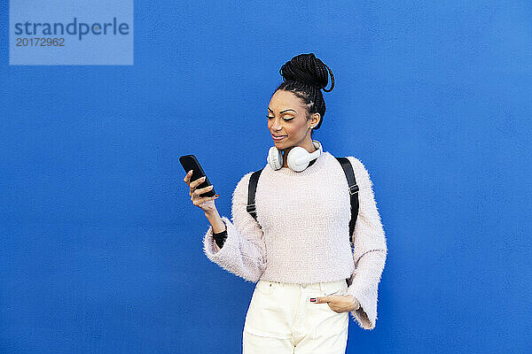 Glückliche junge Frau benutzt Smartphone vor blauer Wand