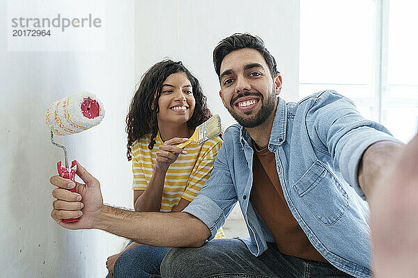 Verspieltes Paar mit Malerausrüstung macht Selfie im neuen Zuhause