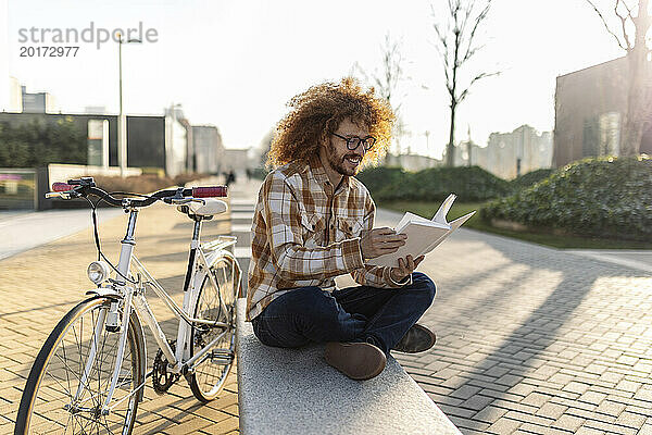 Happy man reading book on seat near bicycle