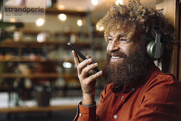 Lächelnder Geschäftsmann mit kabellosen Kopfhörern  der Musik hört und sein Smartphone in der Hand hält