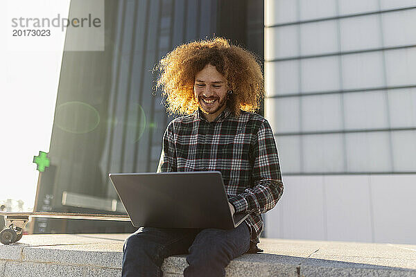 Lächelnder Freiberufler  der vor dem Gebäude am Laptop arbeitet