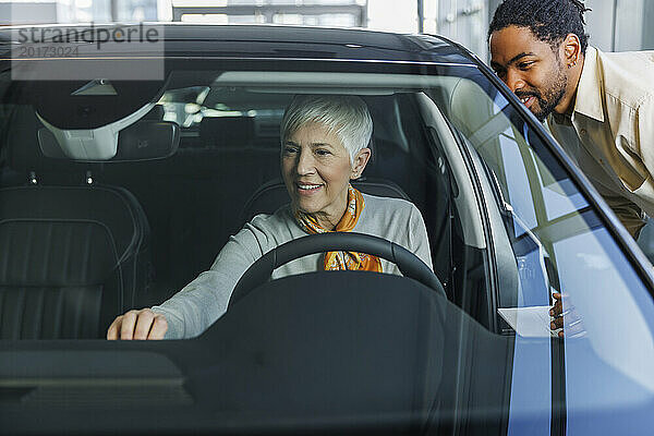 Lächelnder Verkäufer und Frau begutachten Auto im Ausstellungsraum