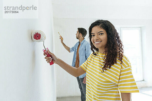Smiling woman with paint roller standing near man at new home