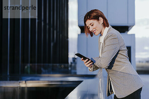 Glückliche Geschäftsfrau nutzt Smartphone in der Nähe von Gebäuden