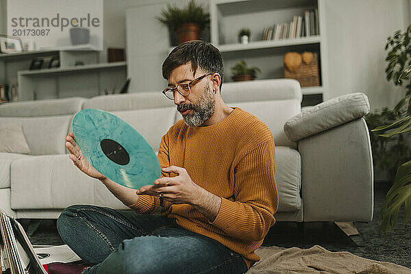 Mann blickt im Wohnzimmer auf altmodische Schallplatte