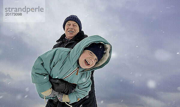 Glücklicher Junge spielt mit Großvater unter dem Himmel im Schnee