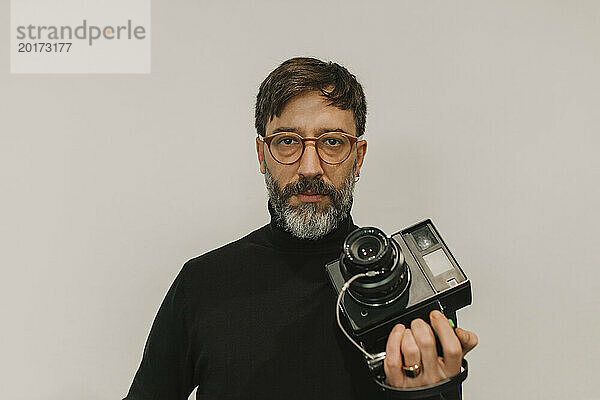 Mann hält alte Sofortbildkamera vor weißem Hintergrund