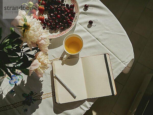 Offenes Tagebuch neben Teetasse und Kirschen auf dem Tisch zu Hause