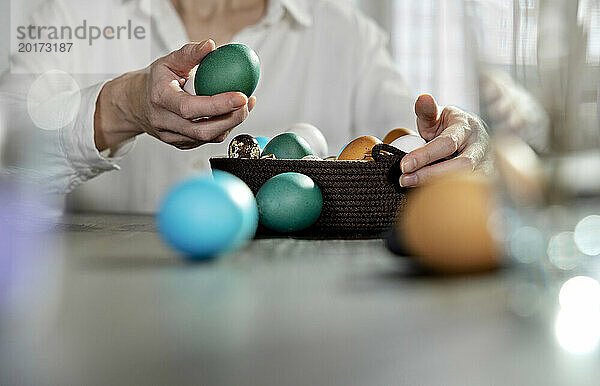 Frau hält grünes Ei im Osterkorb zu Hause