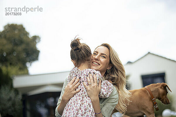 Glückliche Frau umarmt Tochter neben Hund