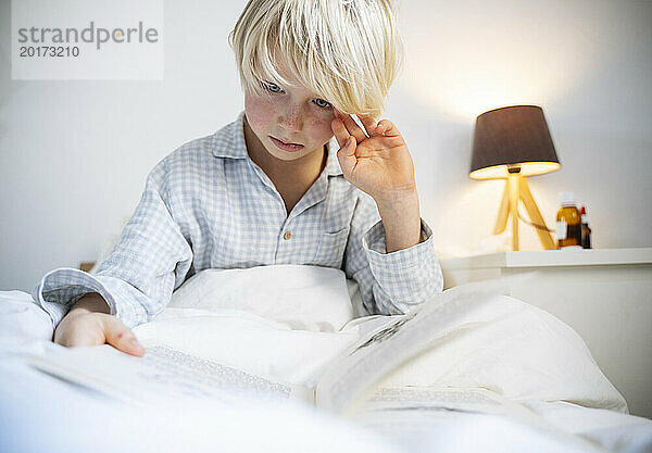 Junge liest Buch im Schlafzimmer zu Hause