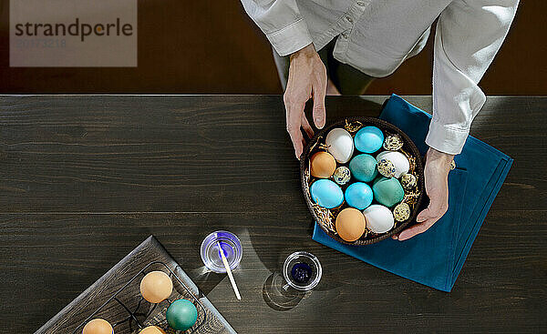 Woman with basket of colorful easter eggs on table at home