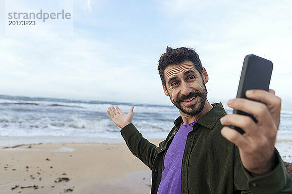 Glücklicher Mann zeigt Strand bei Videoanruf über Smartphone