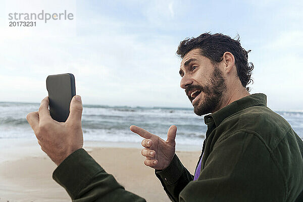 Mann gestikuliert und spricht per Videoanruf über sein Mobiltelefon am Strand