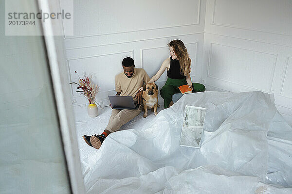 Glücklicher Freiberufler  der am Laptop in der Nähe einer Frau arbeitet  die zu Hause mit Hund sitzt