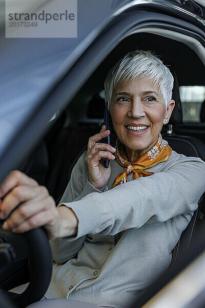 Lächelnde ältere Frau  die im Auto mit dem Smartphone spricht