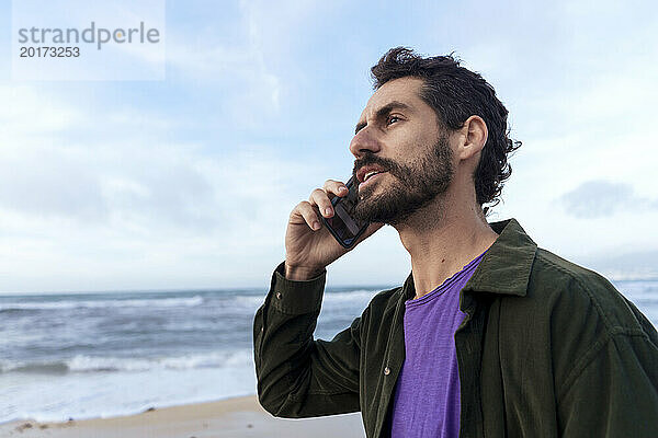 Mann spricht am Strand mit Smartphone