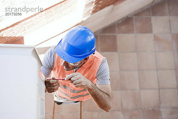 Techniker mit blauem Schutzhelm repariert Klimaanlage in renoviertem Haus