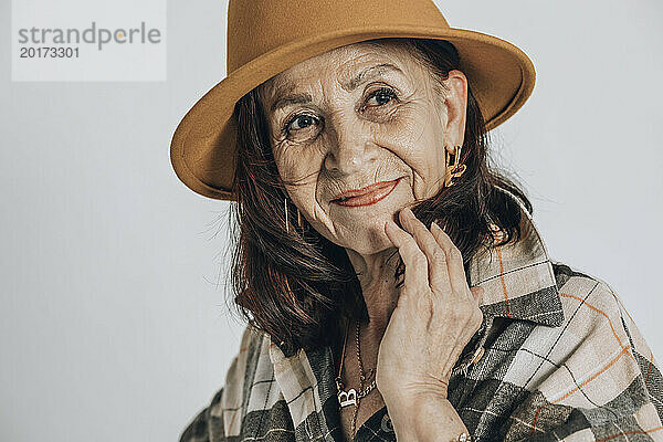 Lächelnde ältere Frau mit Hut vor weißem Hintergrund